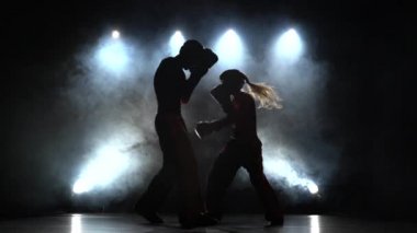 Adam kask ve boks eldivenleri karanlıkta ringde yenerek bir kızla. Arkadan Silhouette.Light. Duman arka plan