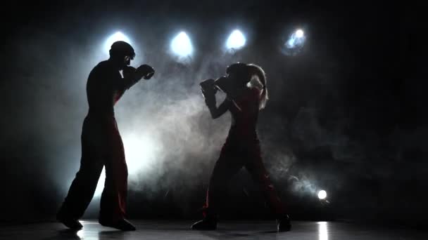 Ragazza sta prendendo a calci un ragazzo con il loro kickboxing sparring. Luce da dietro. Sfondo di fumo. Silhouette — Video Stock