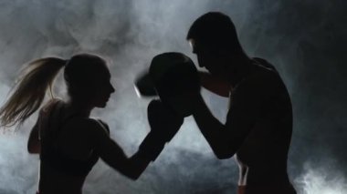 Karanlıkta ringde yenerek kız boks eldivenli adam. Siluet. Duman arka plan. Ağır çekim