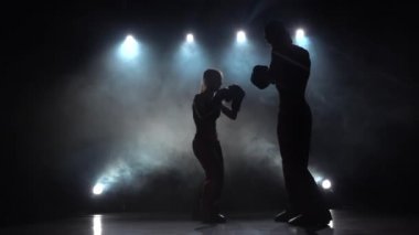 Karanlıkta ringde yenerek adam bir kızla boks eldiven, kickboks rekabet için hazırlanıyorlar. Siluet. Arkadan ışık. Duman arka plan. Ağır çekim
