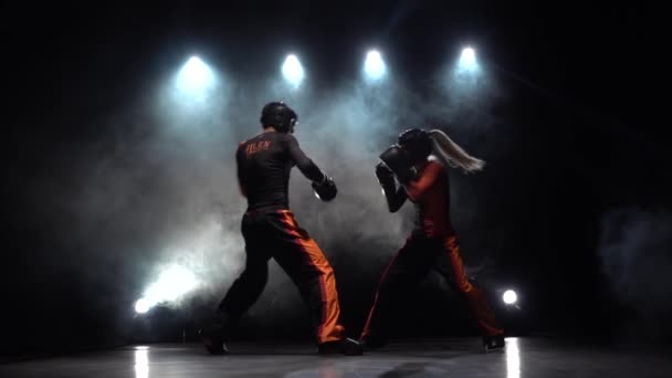 A mulher está a pontapear um tipo com o seu kickboxing. Fundo de fumo. Silhueta. Movimento lento — Vídeo de Stock