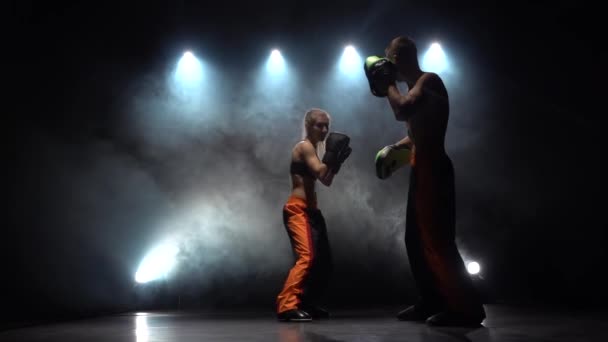 Kerl mit Boxhandschuhen, die im Dunkeln im Ring schlagen, bereiten sie sich auf einen Kickbox-Wettkampf vor. Silhouette. Licht von hinten. Rauchentwicklung. Zeitlupe — Stockvideo