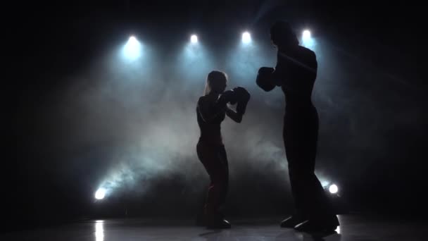 Tipo con una chica guantes de boxeo latiendo en el ring en la oscuridad, se están preparando para una competencia de kickboxing. Silueta. Luz por detrás. Fondo de humo. Movimiento lento — Vídeo de stock