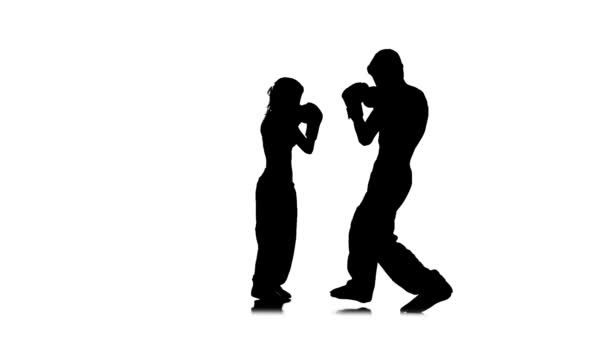 La fille donne des coups de pied au gars qu'ils combattent pour le kickboxing. Silhouette. Fond blanc. Mouvement lent — Video