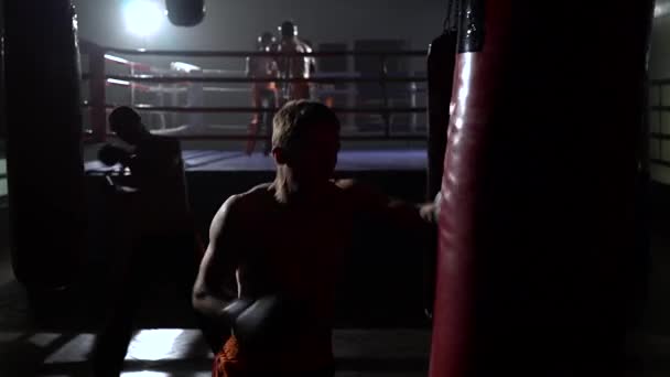 Killar slår ett päron, i bakgrunden i ringen går sparring kickboxers — Stockvideo