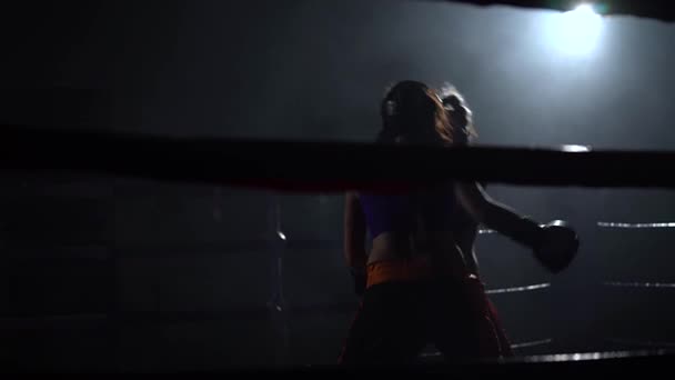 Dos mujeres en cascos boxean sus manos y pies en el anillo en la oscuridad — Vídeos de Stock