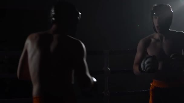 Dos tipos con cascos y guantes de boxeo golpeando en el ring en la oscuridad — Vídeos de Stock