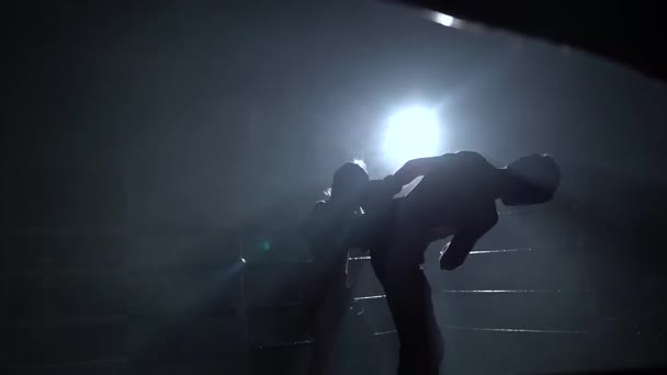 Парень с девушкой в шлемах и боксерских перчатках, бьющимся на ринге в темноте. Силуэт — стоковое видео