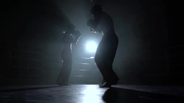 Мужчины с девушкой, избивающей на ринге в темноте. Силуэт — стоковое видео