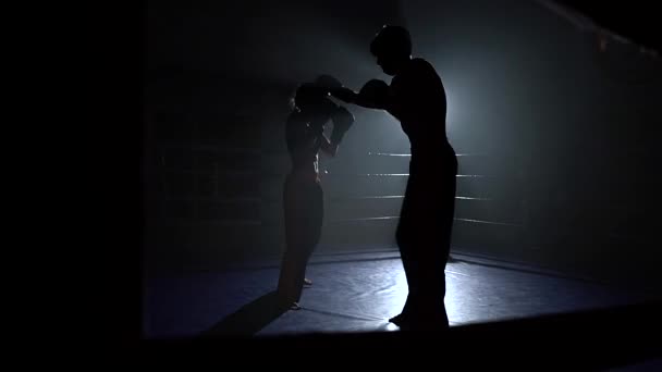 Хлопець з дівчиною в шоломах і боксерських рукавичках б'ється в кільці в темряві. Силует — стокове відео
