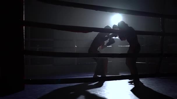 Два парня в шлемах и боксерских перчатках, чтобы сражаться на ринге в темноте — стоковое видео