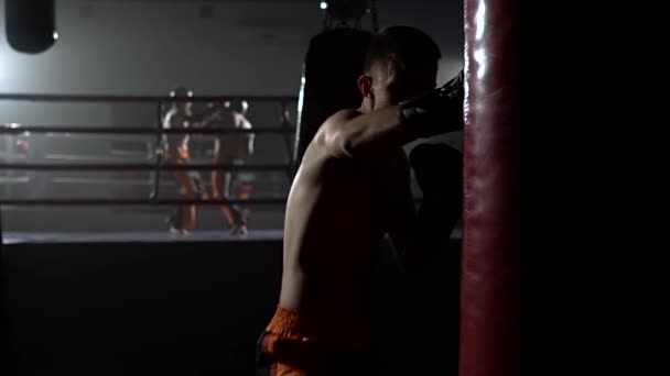 Mann in Handschuhen schlägt eine Birne, im Hintergrund im Ring ein Sparring von Kickboxern. Zeitlupe — Stockvideo