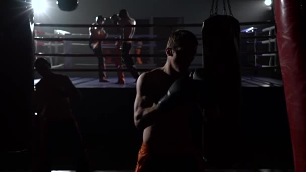 Mann in Handschuhen schlägt eine Birne, im Ring steht ein Sparring von Kickboxern. Zeitlupe — Stockvideo