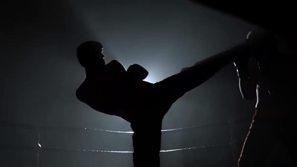 Dos tipos con cascos y guantes de boxeo para luchar en el ring en la oscuridad. En cámara lenta. Silueta — Vídeos de Stock