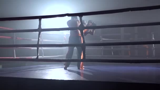 Twee jongens in helmen en bokshandschoenen om te vechten in de ring in het donker. Slow motion — Stockvideo