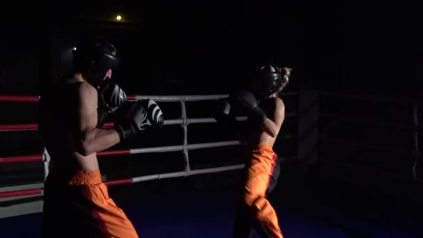 Guy with a girl in helmets and boxing gloves beating in the ring in the dark . Slow motion — Stock Video