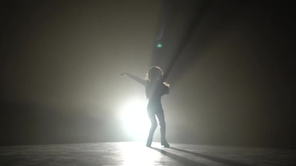 子は、スタジオでエネルギッシュな動きを踊っています。黒い煙の背景。シルエット。後ろからの光 — ストック動画