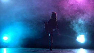 Kız anlamına gelir ve bacağını yukarı yükseltir. Çok renkli duman arka plan. Siluet. Arkadan ışık. Ağır çekim