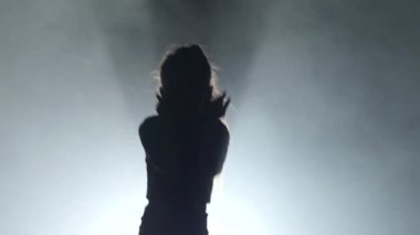 Çocuk dans ediyor ve bacağını yukarı yükseltir. Siyah duman arka plan. Siluet. Arkadan ışık. Ağır çekim. YP kapatın