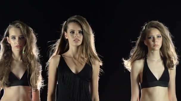 Tři modely ukazují šaty. Černé pozadí. Zpomalený pohyb