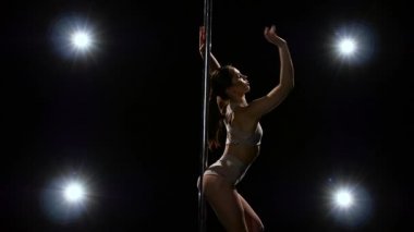 Pole akrobatik hareket bir kız tarafından gerçekleştirilir. Siyah arka plan. Ağır çekim. Arka fenerler