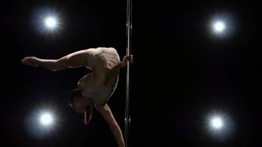 Pole akrobatik hareket bir kız tarafından gerçekleştirilir. Siyah arka plan. Ağır çekim. Arka fenerler