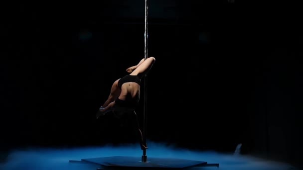 Dancer in a dark studio twirl on a pole in blue smoke. Black smoke background. Slow motion — Stock Video