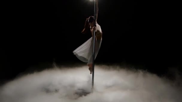 Chica bailando en un poste en un estudio de humo. Fondo de humo negro. Movimiento lento — Vídeo de stock