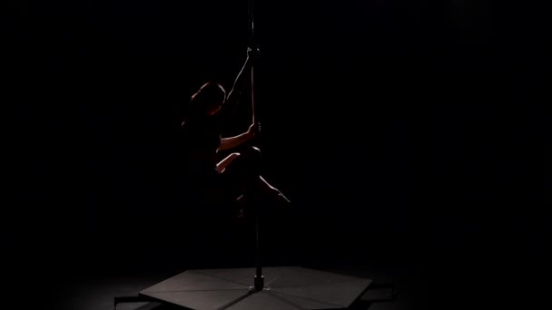 Striptease spins on a pole in the studio . Black background. Slow motion. Silhouette — Stock Video