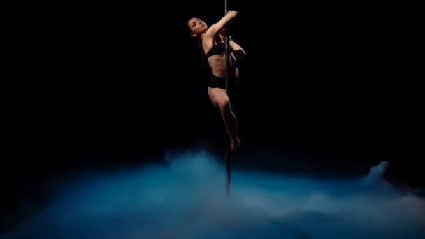 Bailarina en un oscuro estudio girando sobre un poste de humo azul. Fondo de humo negro. Movimiento lento — Vídeo de stock