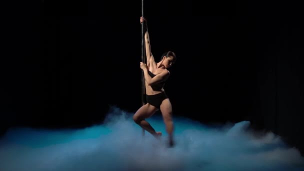 Girl with flowing hair dancing on a pole in a dark smoky room. Black background — Stock Video