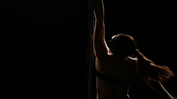 Bailarina en ropa interior girando en un poste. Fondo negro. Silueta. De cerca. — Vídeos de Stock
