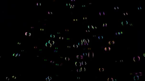 Мыльные пузыри летят и исчезают в разных цветах. Чёрный фон — стоковое видео