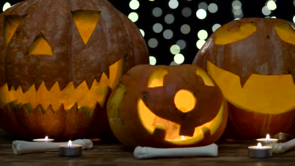 Las caras aterradoras de las calabazas en Halloween son huesos al lado de ellas. Fondo negro bokhe. De cerca. — Vídeo de stock
