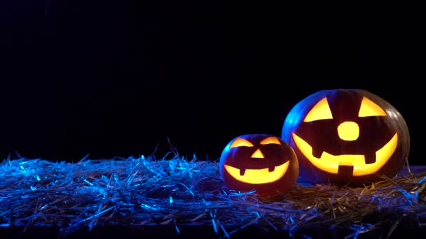 Dos calabazas de Halloween están ardiendo llamas brillantes en el interior están de pie sobre el heno. Fondo negro — Vídeos de Stock