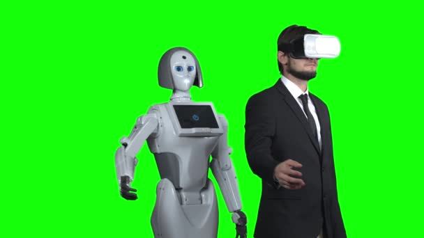Der Mann mit der Virtual-Reality-Brille legt die Hand zur Seite und der Roboter wiederholt sich hinter ihm. Green Screen — Stockvideo