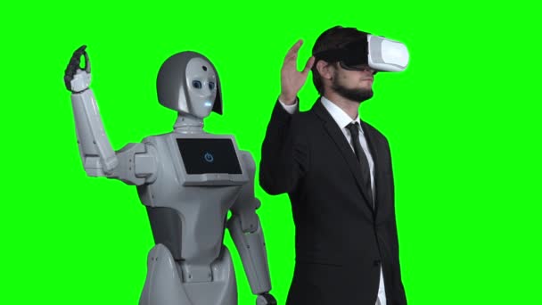 Facet z okulary wirtualnej rzeczywistości podnosi rękę w górę i fale robot powtarza za nim. Zielony ekran. Zwolnionym tempie — Wideo stockowe