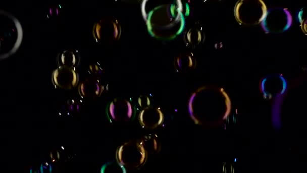 Мыльные пузыри летят и исчезают в разных цветах. Медленное движение. Чёрный фон — стоковое видео