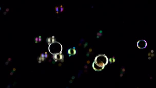 Радужные мыльные пузыри летают. Медленное движение. Чёрный абстрактный фон — стоковое видео