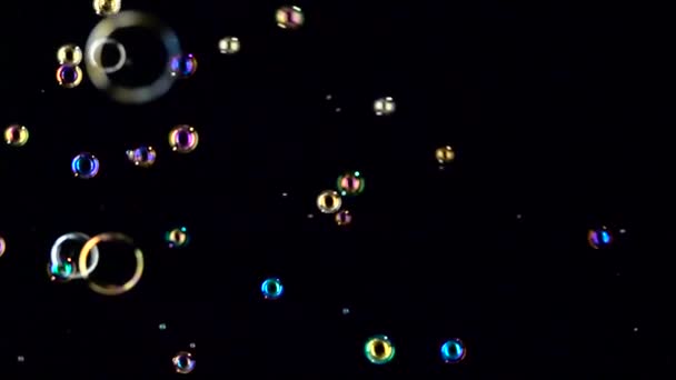 Diferentes tamaños y burbujas de jabón de color vuelan. En cámara lenta. Fondos negros — Vídeo de stock
