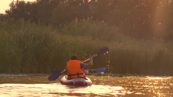 Två personer rodd årorna sitter i en kajak på sjön i solnedgången — Stockvideo