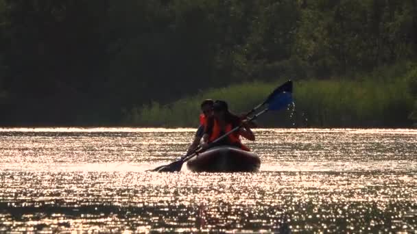 Ragazzo e ragazza che remano lungo il fiume con pagaie sedute in kayak vengono mandati al tramonto. Rallentatore — Video Stock