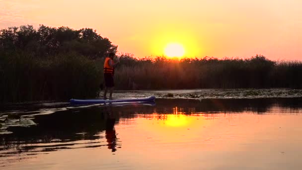 Людина встаньте на дошку весла на надувний пліт на заході сонця. Повільний рух — стокове відео