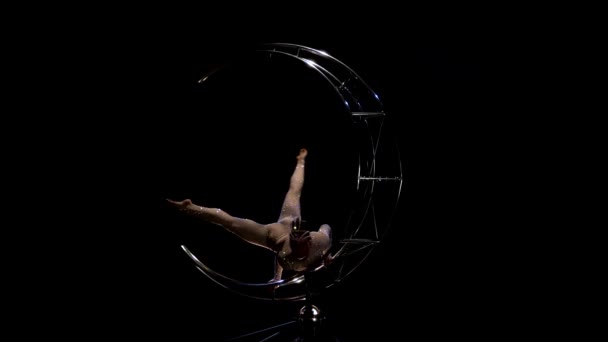 Dziewczynka gimnastyczka na jedno ramię wykonuje wykonując akrobacje na obrotowym księżyc struktury. Czarne tło — Wideo stockowe