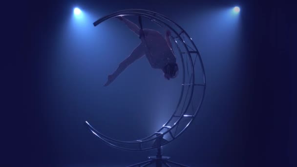Девушка из художественной гимнастики выполняет отбросы на одной руке в воздухе на металлической вращающейся структуре луны. Синий дым — стоковое видео