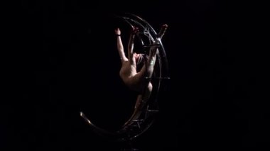 Jimnastikçi bir metal yapının ayda dikey bir dize döndürür. Siyah arka plan