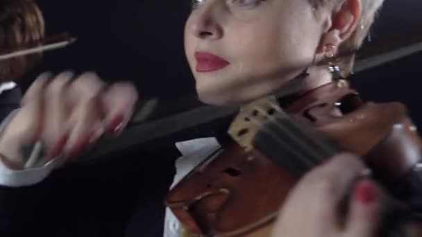 Girls in play the violins in a composition in a room. Black background. Close up — Stock Video