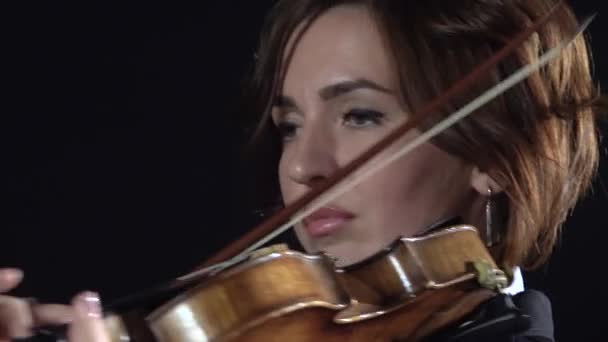 La chica se inclina sobre las cuerdas de un violín. Fondo negro. De cerca. — Vídeos de Stock