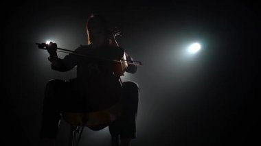 Bir çello fener ile karanlık bir stüdyoda bir müzisyenle silüeti. Siyah duman arka plan