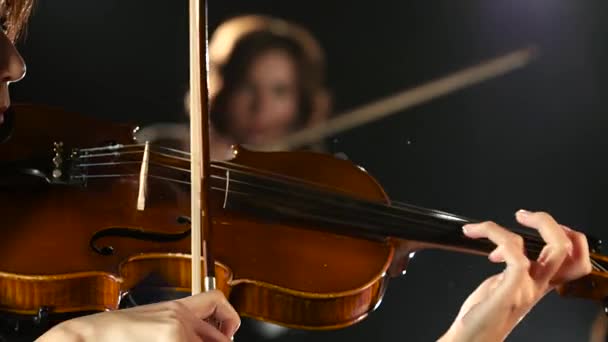 Kvinnor bågar över strängarna på en fiol i ett rum. Svart bakgrund. Närbild — Stockvideo